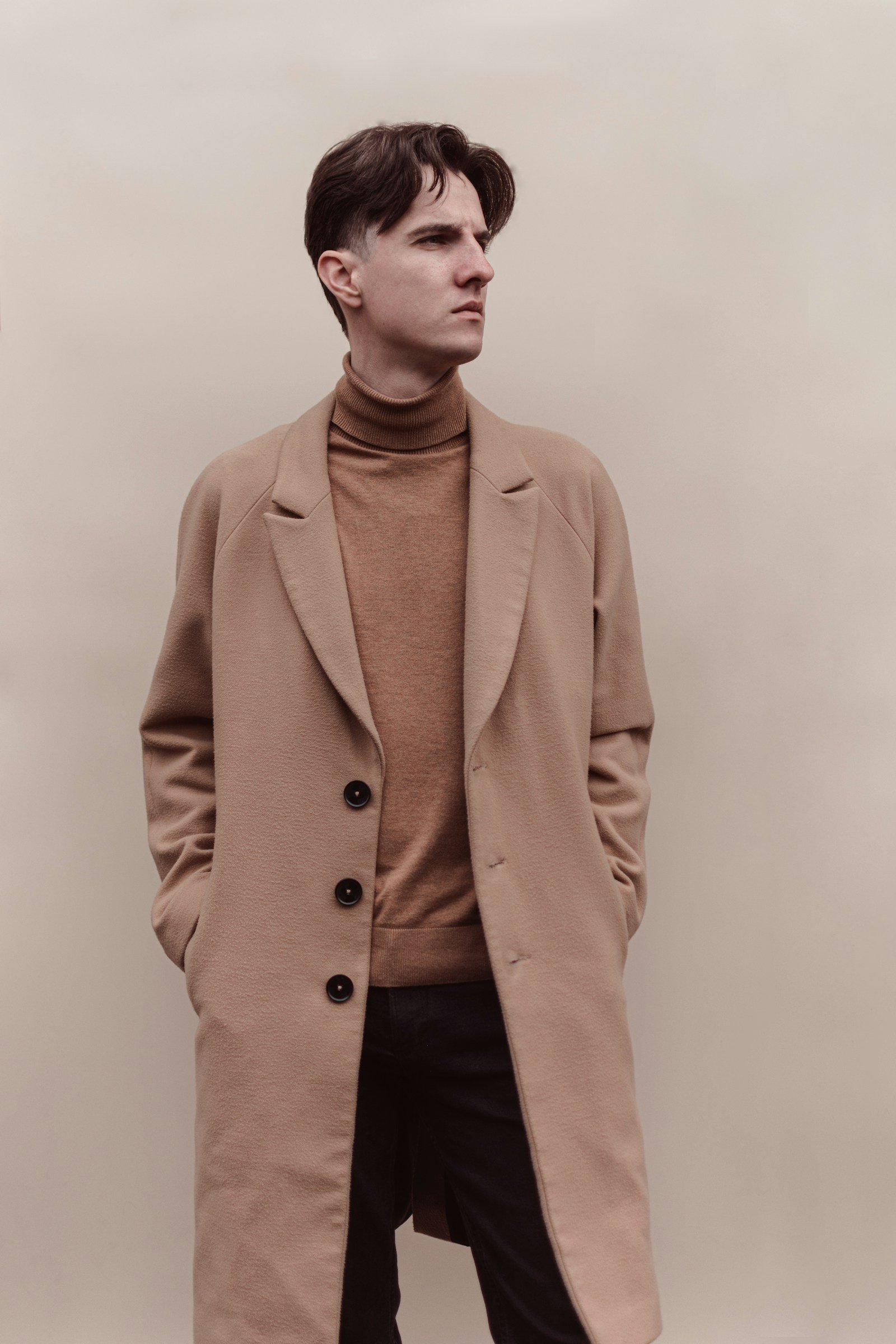 Man wearing a camel overcoat against a warm neutral wall